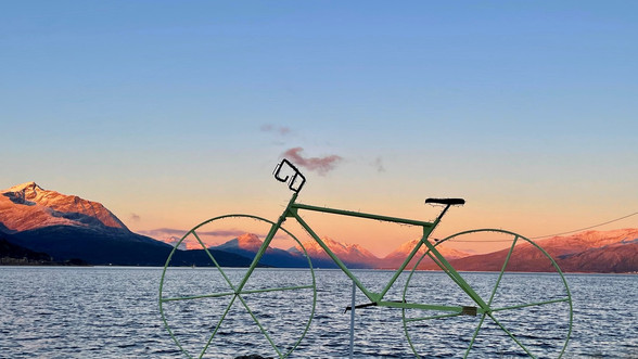 Grønn sykkel foran fjord og fjell. Himmel som er blå og rosa i soldnedgangen. Bildet er tatt i Lødingen